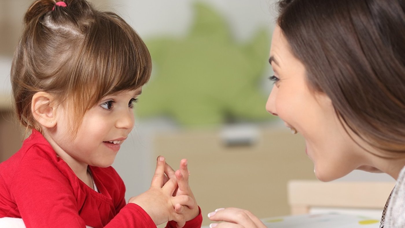 Mother and toddler wearing red shirt playing together on a bed in the bedroom at home