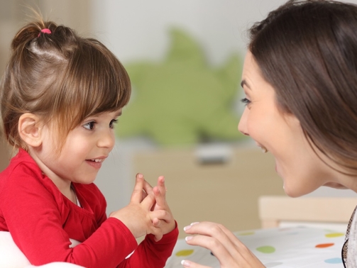Mother and toddler wearing red shirt playing together on a bed in the bedroom at home