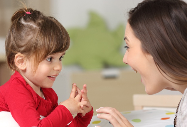 Mother and toddler wearing red shirt playing together on a bed in the bedroom at home